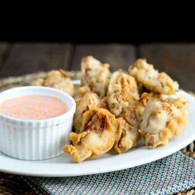 A plate of fried mushrooms and artichoke hearts served with a cup of creamy spiced aioli on the side.