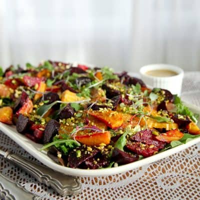 Colorful Roasted Beet and Citrus Salad with greens and chopped pistachios, artfully served on a white platter.