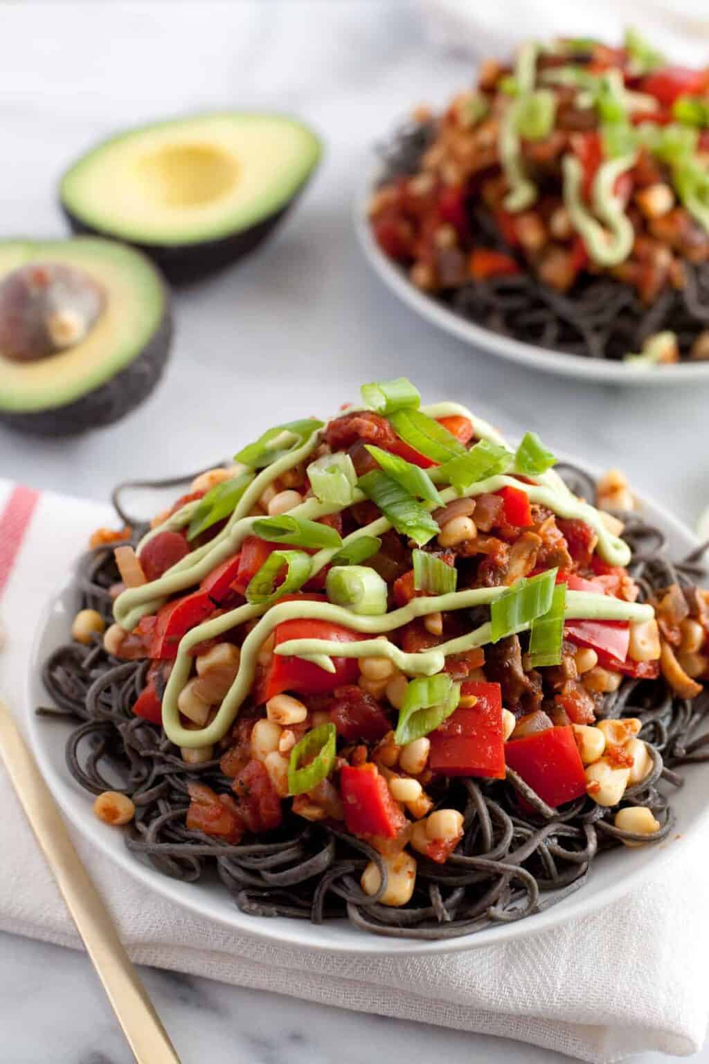 Black bean pasta with avocado cream sauce lime cilantro cherry tomatoes and cotija in a bowl