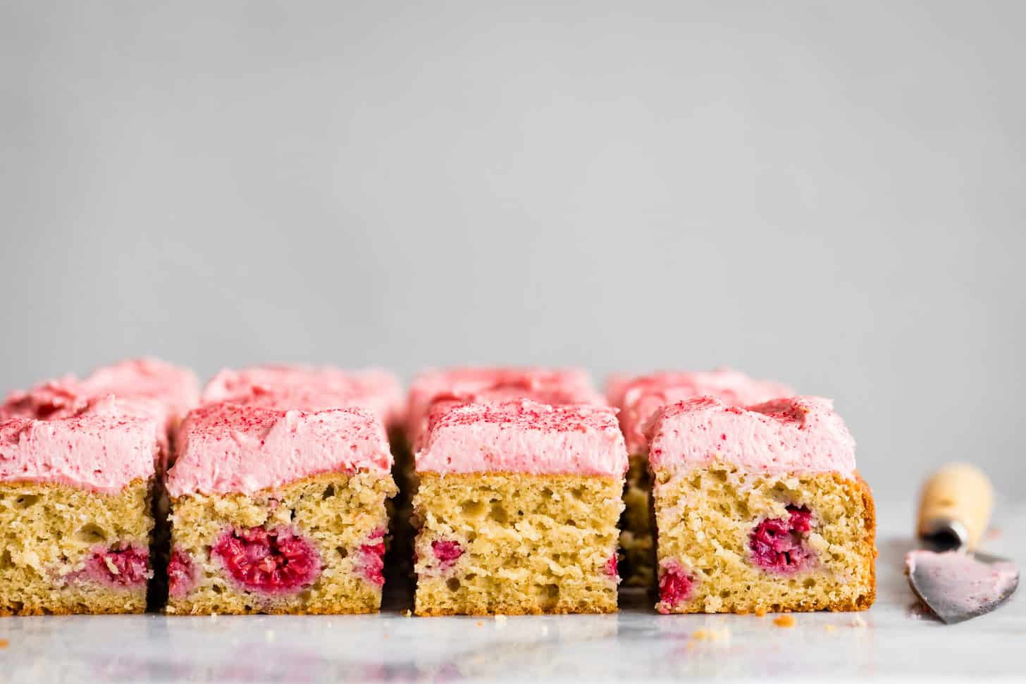 Sliced raspberry cake squares with pink frosting lined up on a white surface