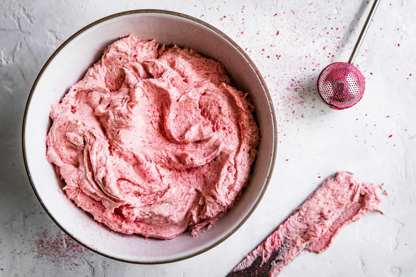 A bowl of pink whipped raspberry cream cheese frosting with offset spatula
