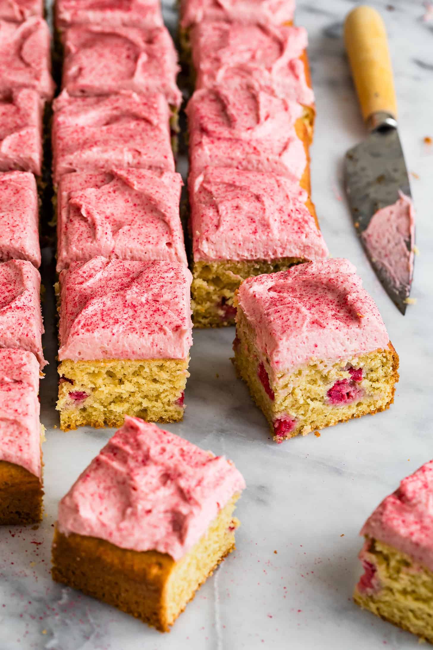 Sliced raspberry cake with pink frosting and fresh raspberries on a marble surface