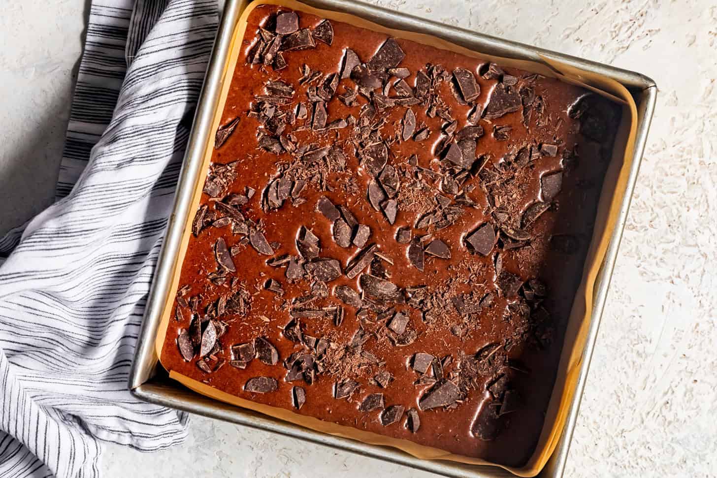 Unbaked mochi brownies in baking pan with chocolate on top