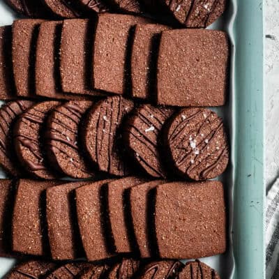 Rows of square and round chocolate cookies, some drizzled with chocolate and sprinkled with sea salt, are joined by classic No-Bake Peanut Butter Cookies for a delightful mix of textures and flavors.