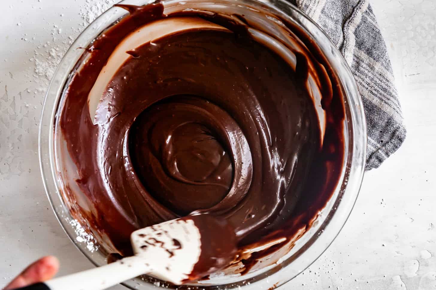 A bowl of chocolate icing for a Fudgy Texas Sheet Cake being mixed with a spatula