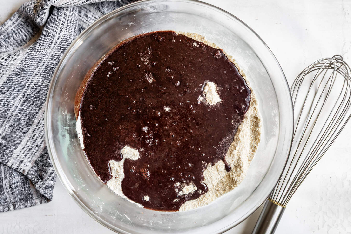 Pouring Cocoa and Butter into Dry Ingredients in Glass Bowl with Whisk