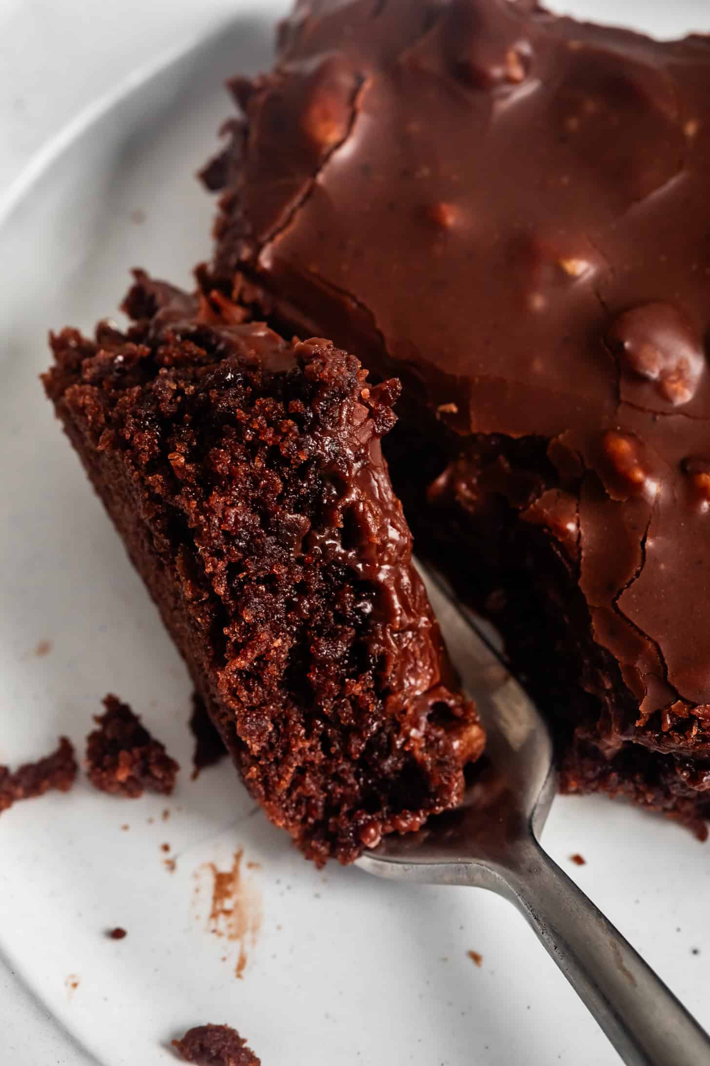 A close-up of a fork cutting into a rich and moist Gluten-Free Texas Sheet Cake with glossy chocolate icing.