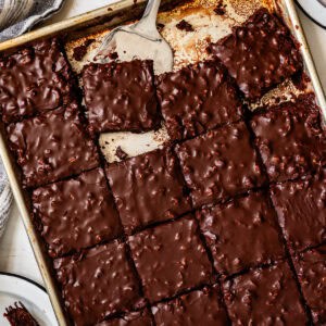 A baking sheet of fudgy Gluten-Free Texas Sheet Cake brownies, cut into squares, with a spatula lifting one piece