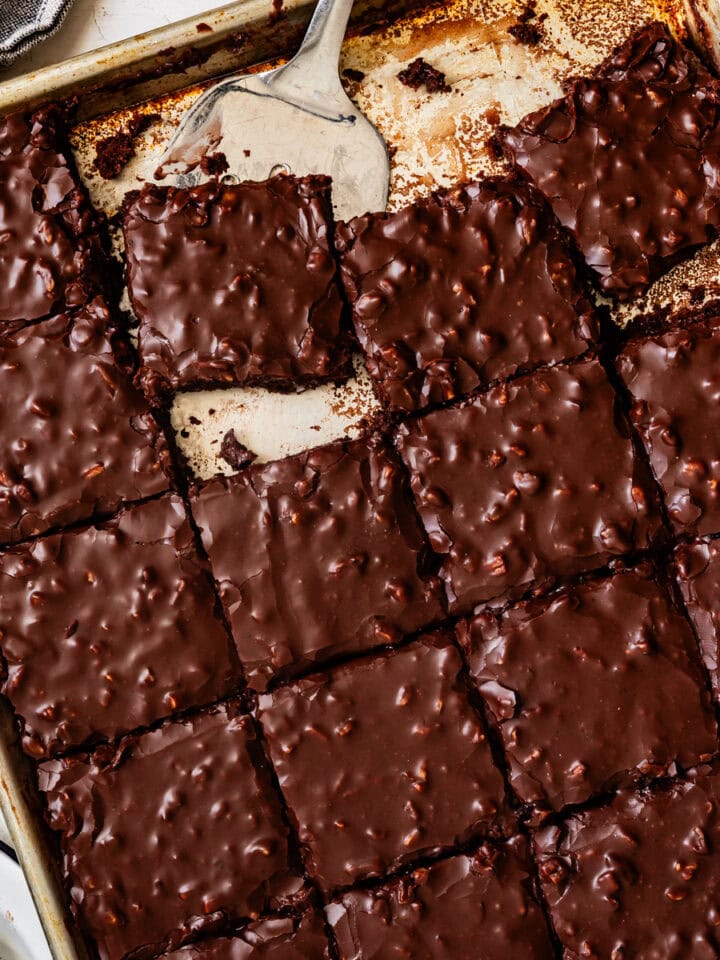 A baking sheet of fudgy Gluten-Free Texas Sheet Cake brownies, cut into squares, with a spatula lifting one piece