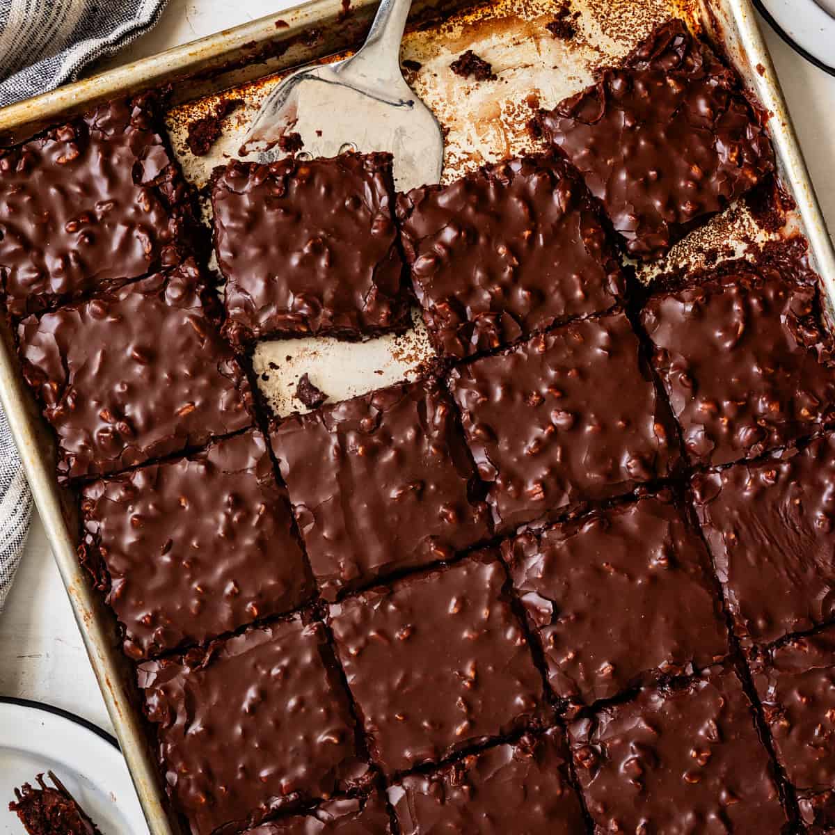 A baking sheet of fudgy Gluten-Free Texas Sheet Cake brownies, cut into squares, with a spatula lifting one piece