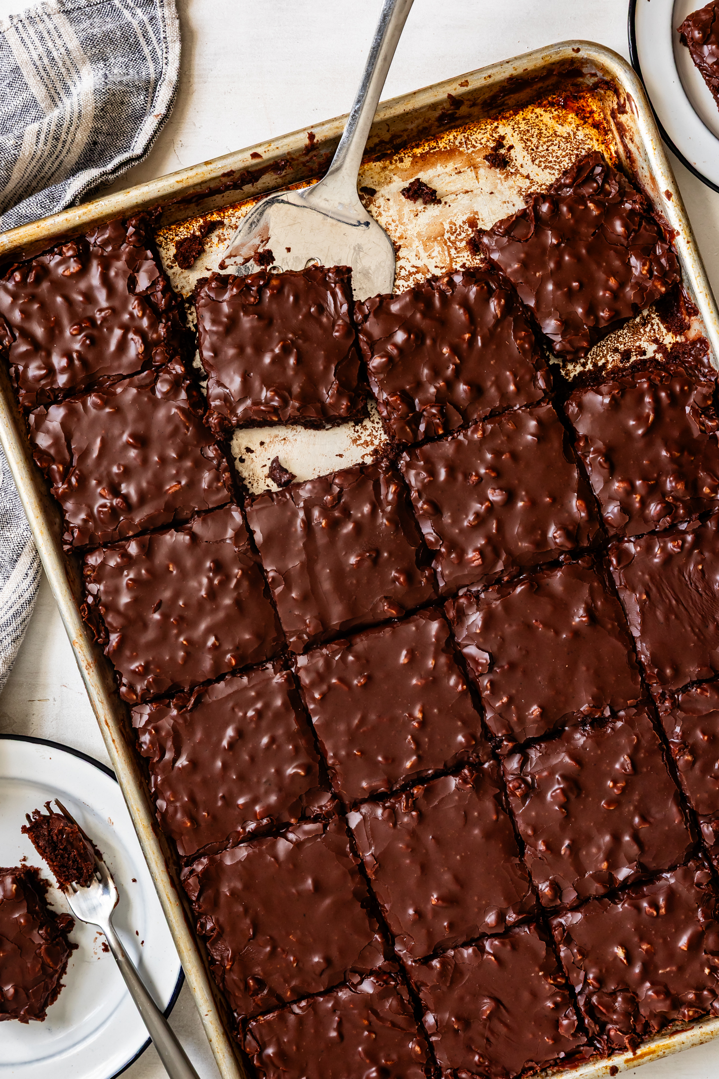 A baking sheet of fudgy Gluten-Free Texas Sheet Cake brownies, cut into squares, with a spatula lifting one piece