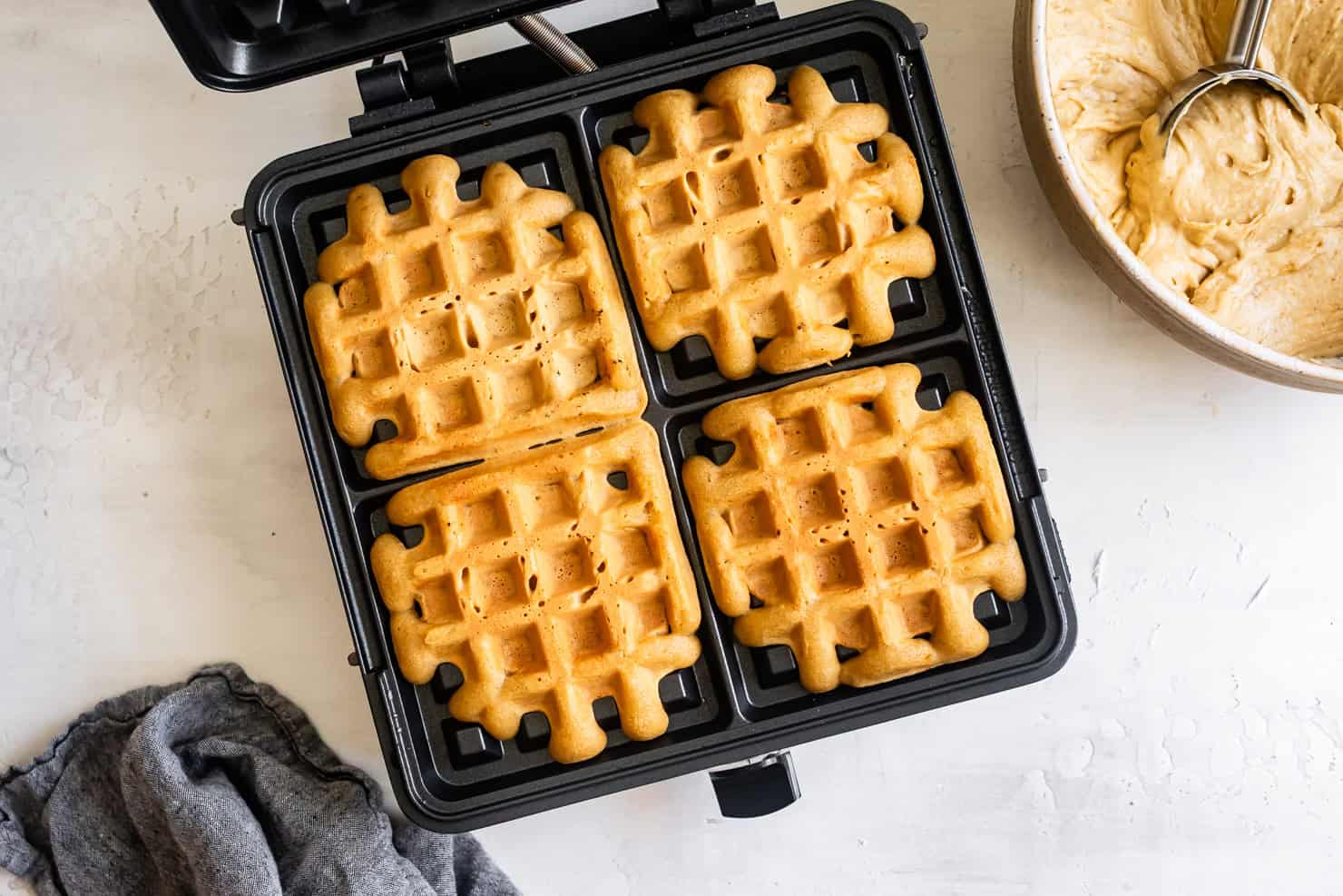 Four mochi waffles in a waffle maker next to a bowl of sweet mochi waffle batter
