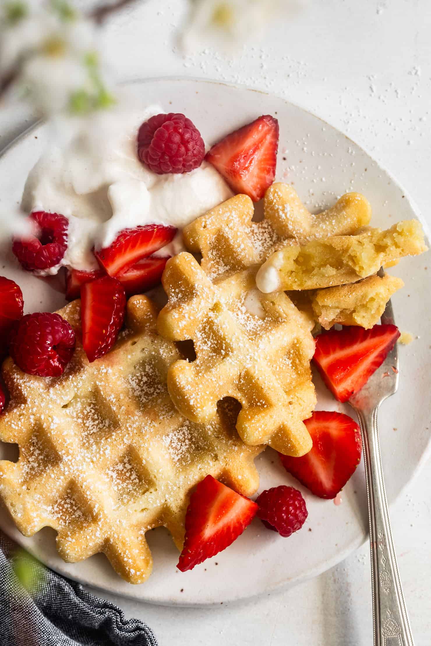 Chewy mochi waffles with powdered sugar, strawberries, raspberries, and whipped cream on a plate with a fork.