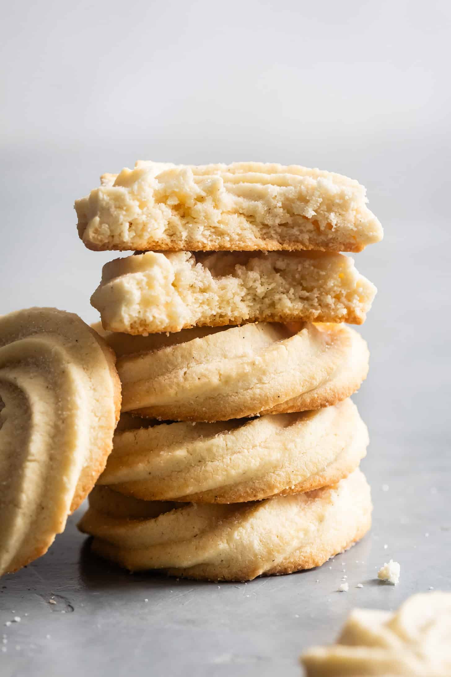 A stack of round gluten-free butter cookies, with one cookie on top broken in half to reveal the crumbly texture.