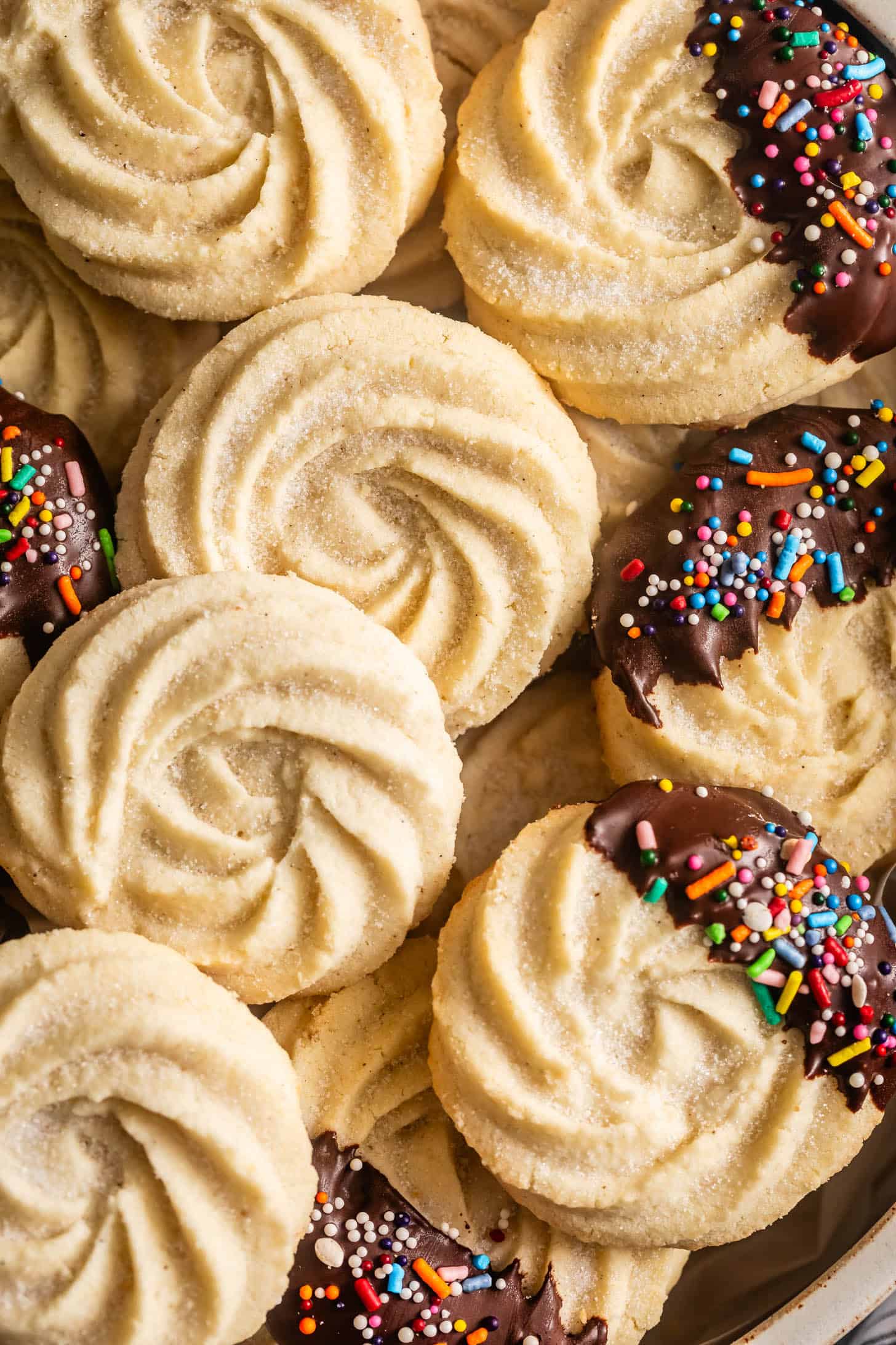 A close-up of gluten-free butter cookies made with almond flour, some dipped in chocolate and covered with colorful sprinkles.