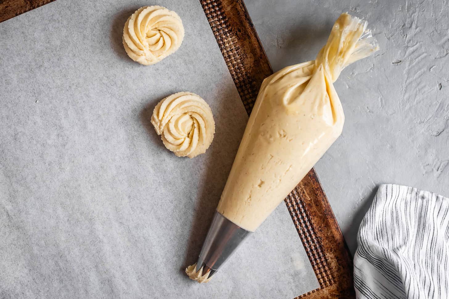 A piping bag with almond flour butter cookie dough and two piped butter cookie shapes on parchment paper