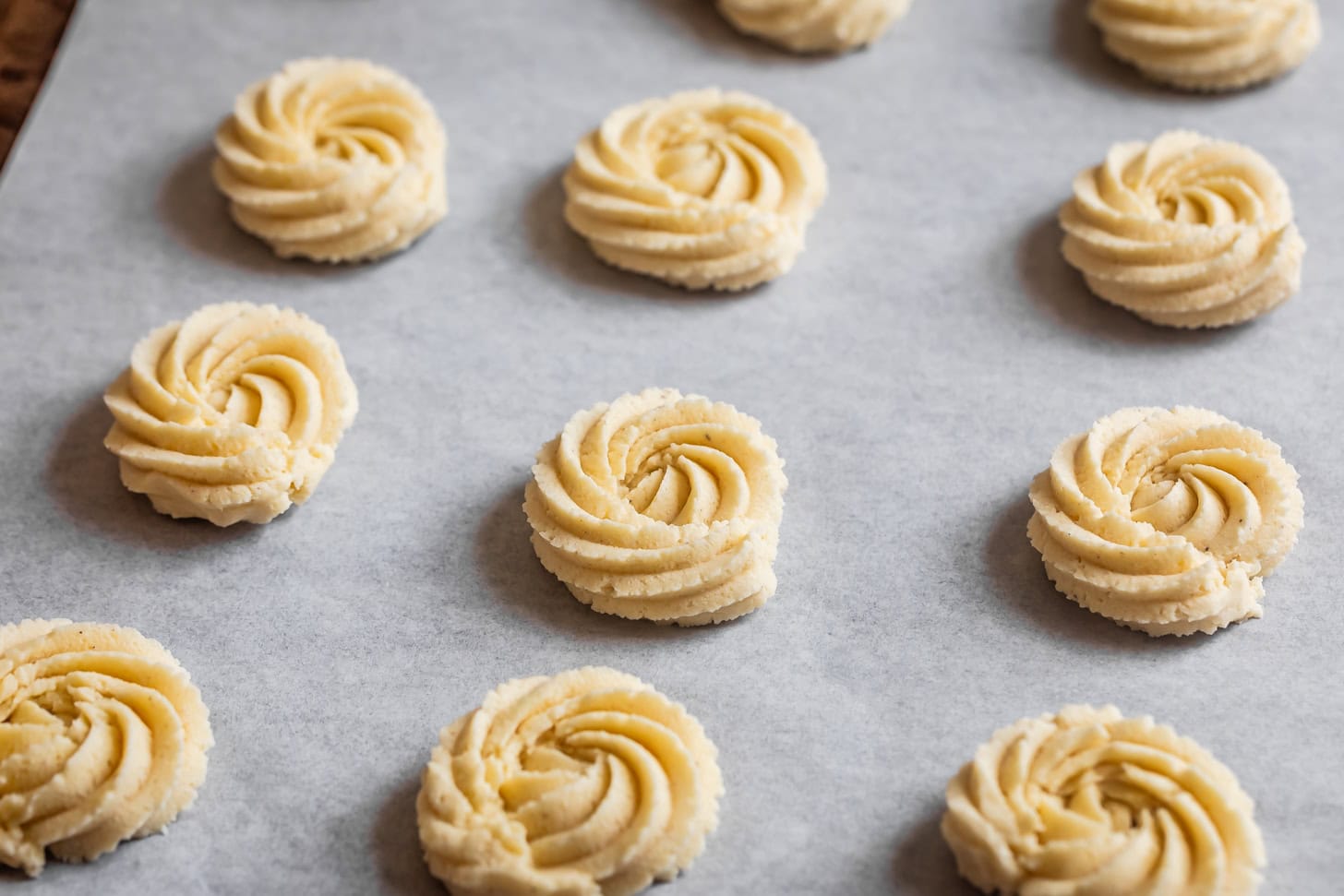Unbaked gluten-free butter cookies, made with almond flour, arranged on a parchment-lined baking sheet.