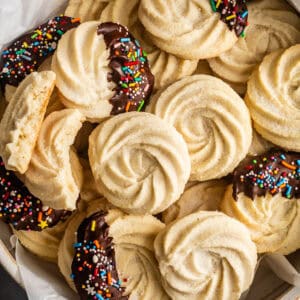 A close-up pile of swirled gluten-free butter cookies, some dipped in chocolate and sprinkles.