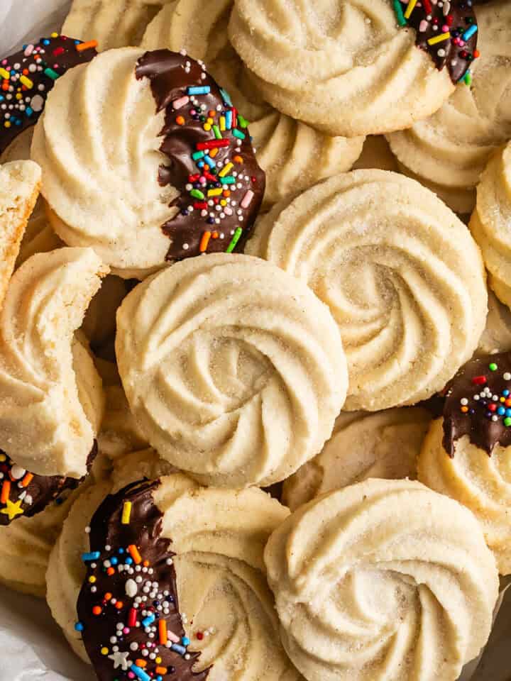 A close-up pile of swirled gluten-free butter cookies, some dipped in chocolate and sprinkles.